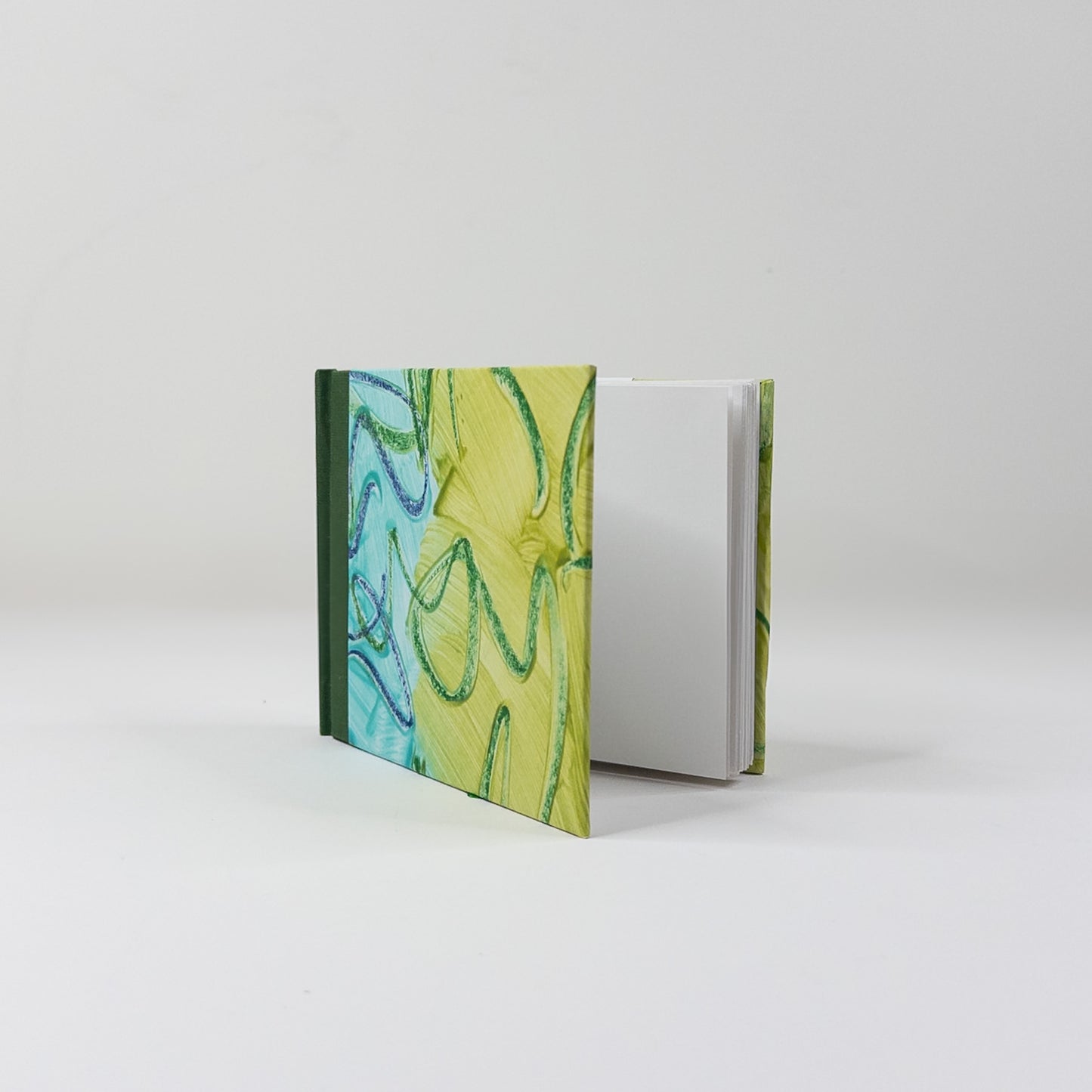 Landscape handmade sketchbook standing upright, showing blank pages and green cloth spine