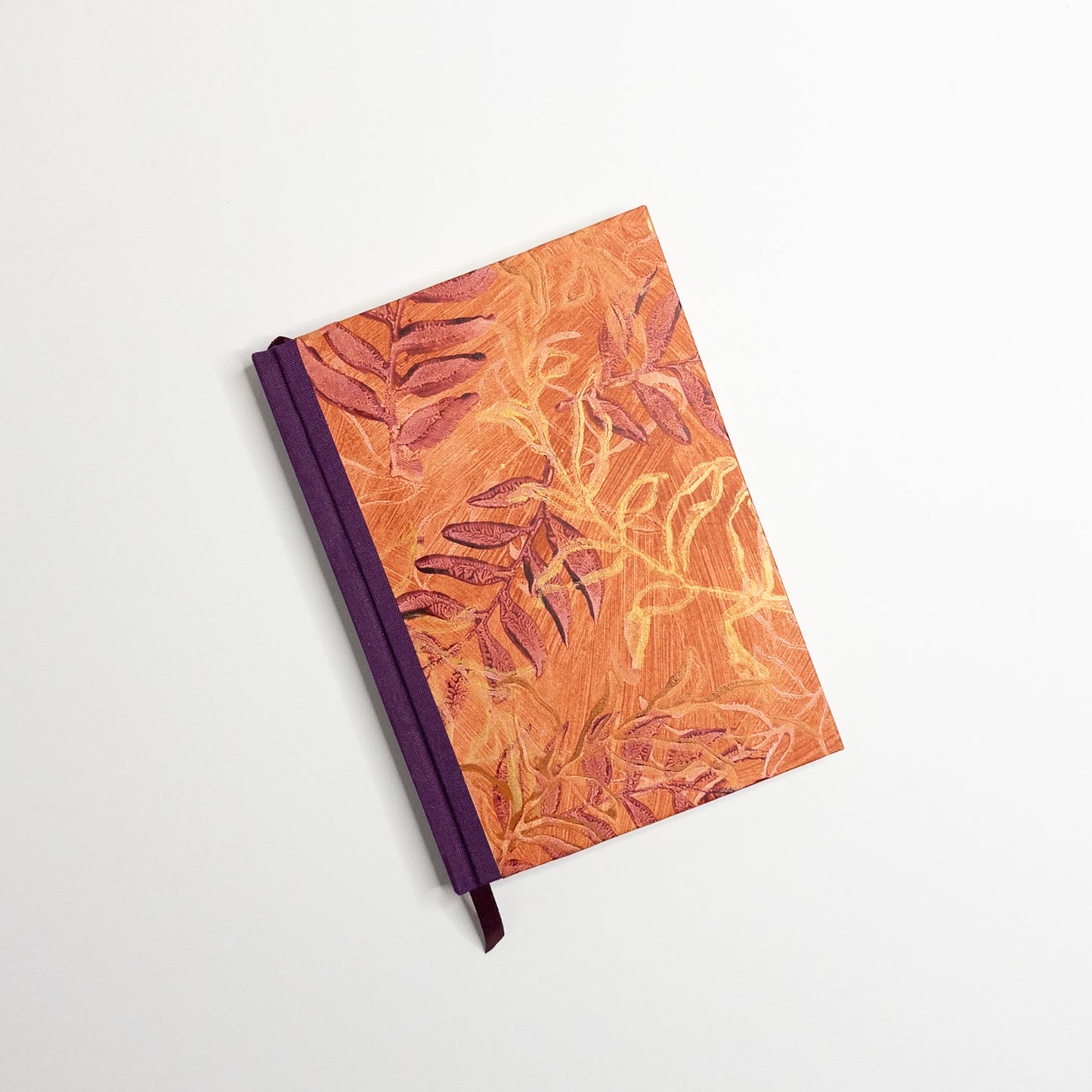 Orange paste paper cover printed with burgundy and gold leaves, purple book cloth spine and ribbon marker, hand bound by Patti Paulus