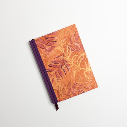 Orange paste paper cover printed with burgundy and gold leaves, purple book cloth spine and ribbon marker, hand bound by Patti Paulus