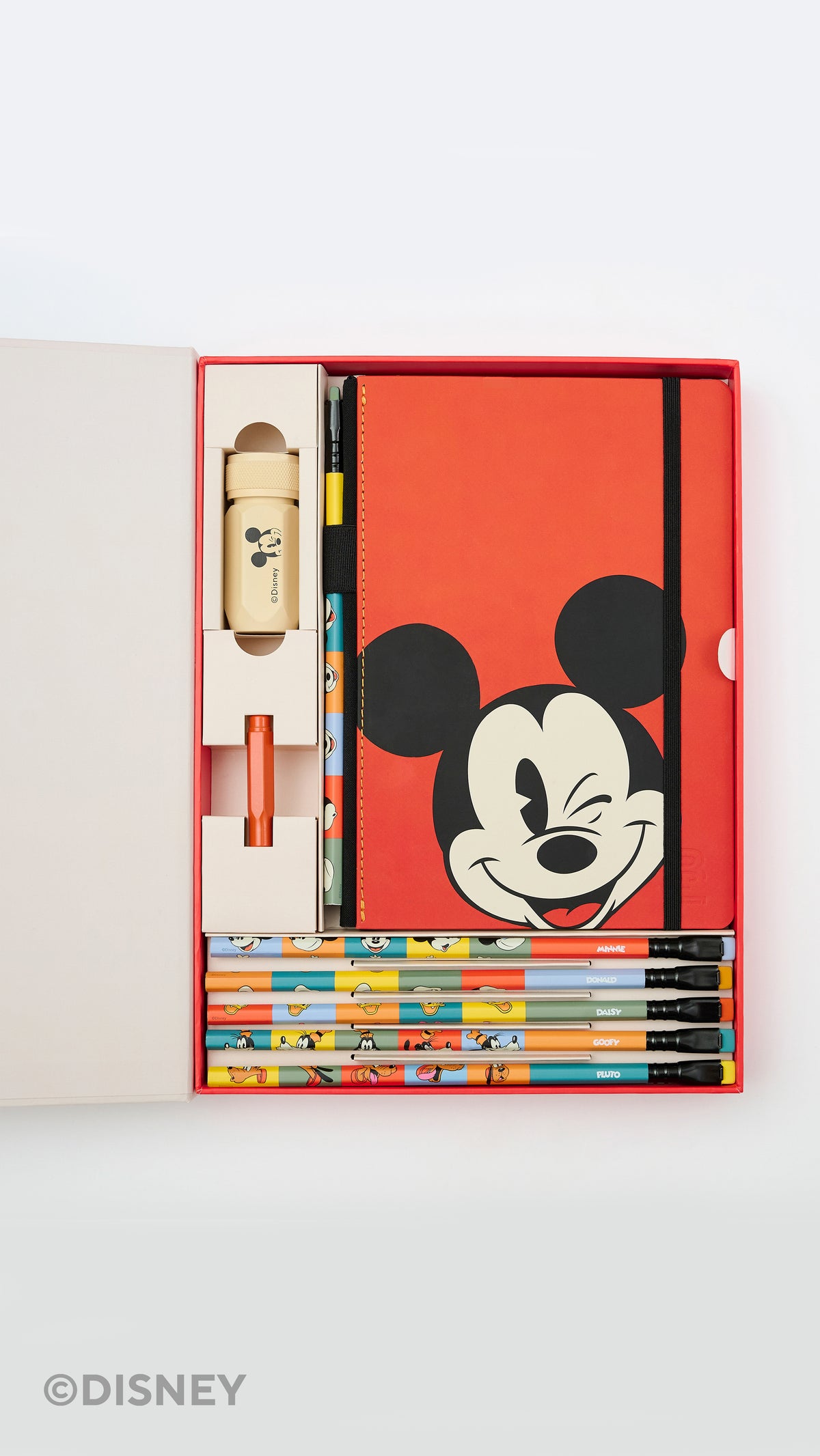 A Disney stationery gift set displayed in an open red box on a light gray background. The set includes a red notebook with a large Mickey Mouse face, several colorful pencils, a small beige bottle or container, and other stationery items.